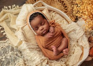 Sleeping newborn wrapped in caramel swaddle in white basket with lace blanket.