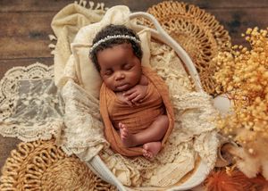 Sleeping newborn wrapped in rust swaddle with cream lace in a wicker basket with autumn floral decor.