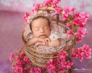 Newborn baby sleeping in a wicker basket adorned with pink cherry blossoms wearing a lace bonnet.