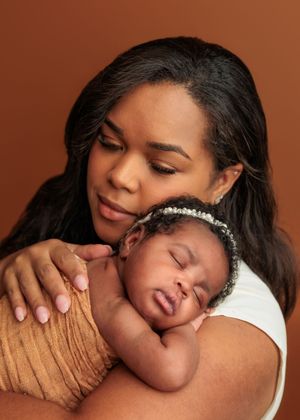 Mother with long dark hair gazing lovingly at sleeping newborn baby girl.