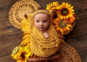 Alert newborn baby wrapped in yellow with sunflowers on wooden background.