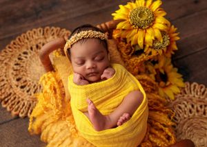 Newborn baby swaddled in yellow wrap resting in basket surrounded by bright sunflowers.