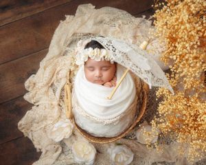 Peaceful newborn baby swaddled in white wrap sleeping in wicker basket with golden floral decor.