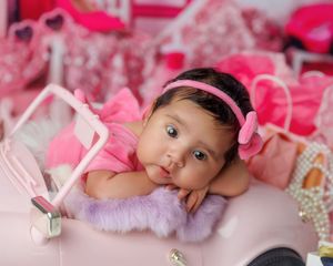 Adorable baby girl in pink outfit with bow headband posing in pink toy car.