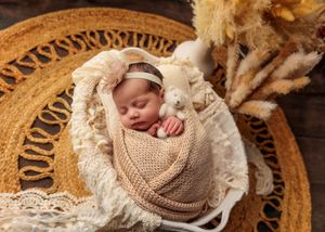 Sleeping newborn in beige knit wrap in wicker basket with boho pampas decor.