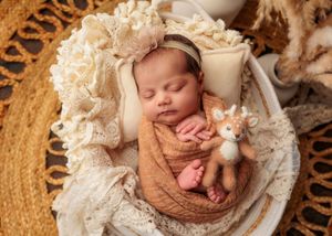 Newborn baby in caramel wrap with lace headband cuddling a deer stuffed animal.