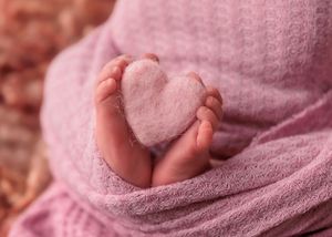 Close-up of newborn baby feet wrapped in pink blanket holding a small felt heart.