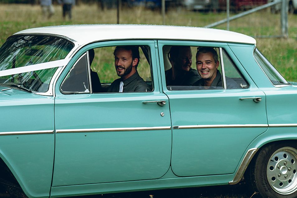 Two people sitting in a vintage mint green sedan car on a sunny day.