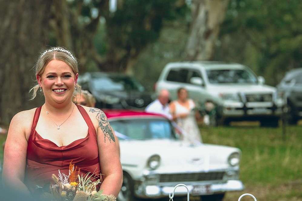 A person in a burgundy top holds a bouquet of white and pink flowers at an outdoor event.