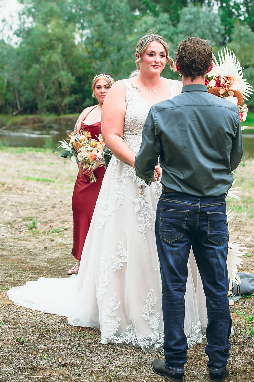 A sweet moment at an outdoor wedding as a young ring bearer in jeans hugs the bride's flowing lace dress.