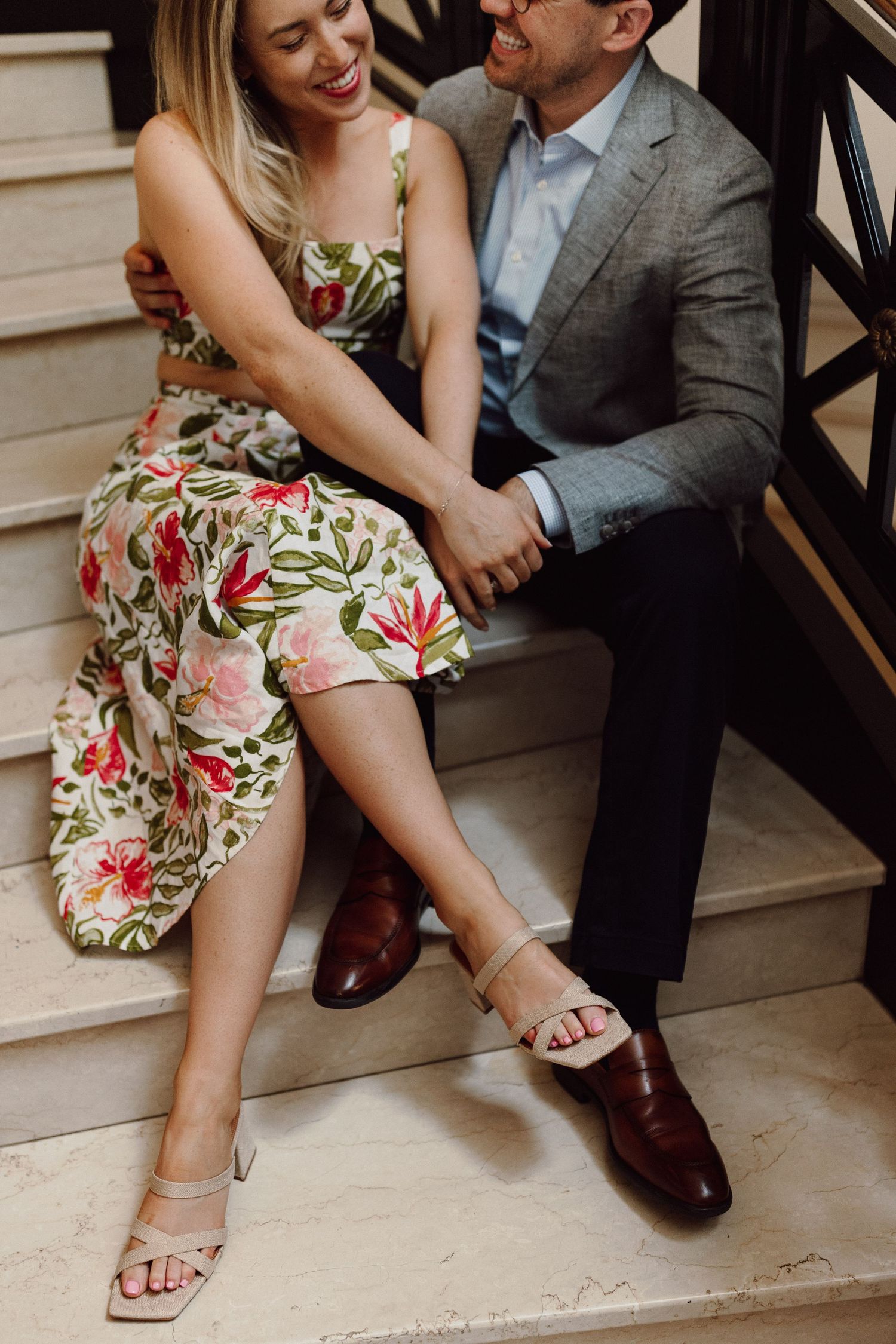 Couple sitting on stairs showing playful interaction, with focus on floral dress and formal attire.