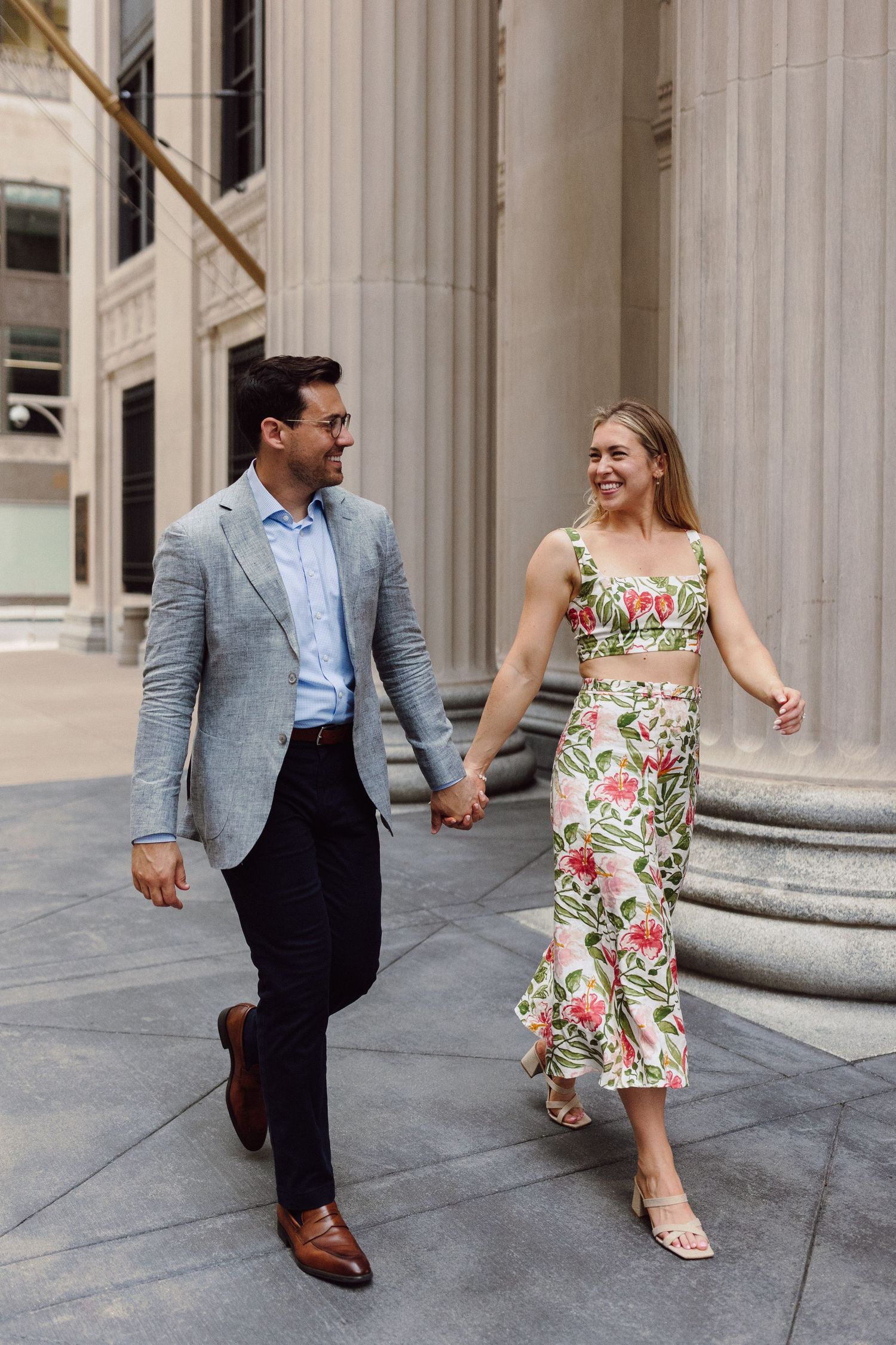 Couple in formal attire playfully interacting near classical columns of a building.