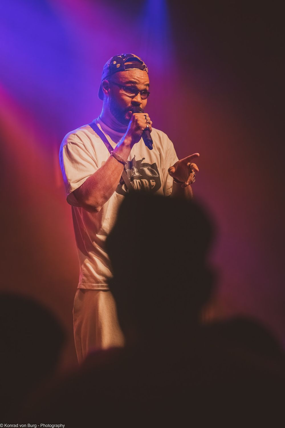 Concert performer on stage with colorful purple and red lighting effects.