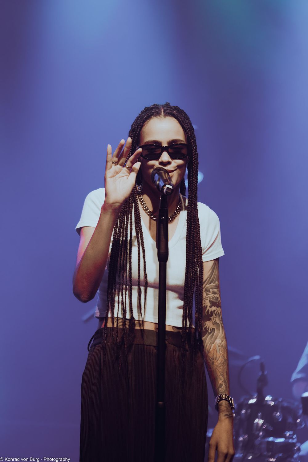 Concert performer with long braids singing against blue stage lighting.