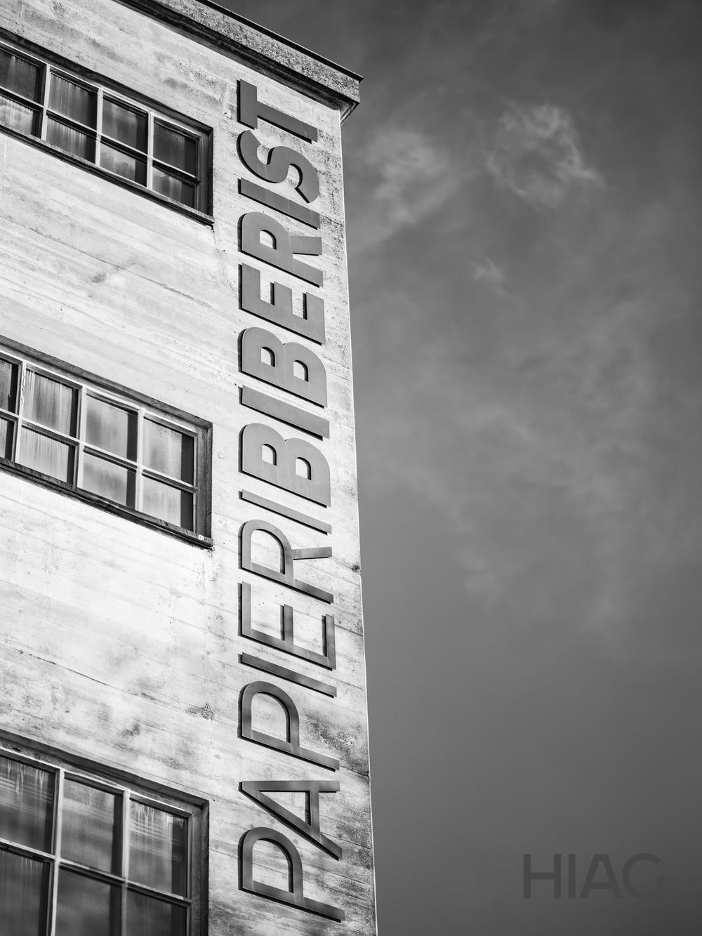 Black and white architectural photo of Papierberst building facade with windows against cloudy sky.