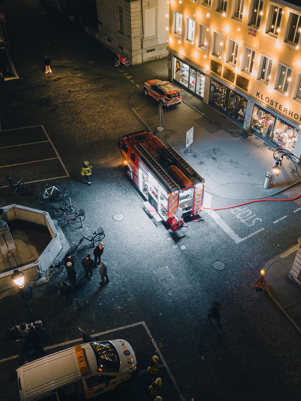 Aerial night view of emergency vehicles and responders at an illuminated urban scene.