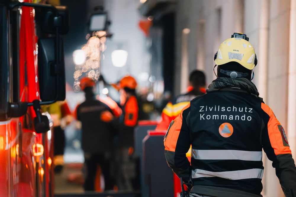 Emergency responder in reflective gear with Zivilschutz Kommando text on uniform at night scene.