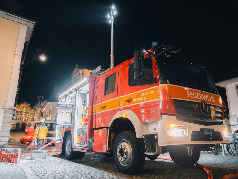 Red fire truck parked on city street at night with emergency lights illuminating the scene.