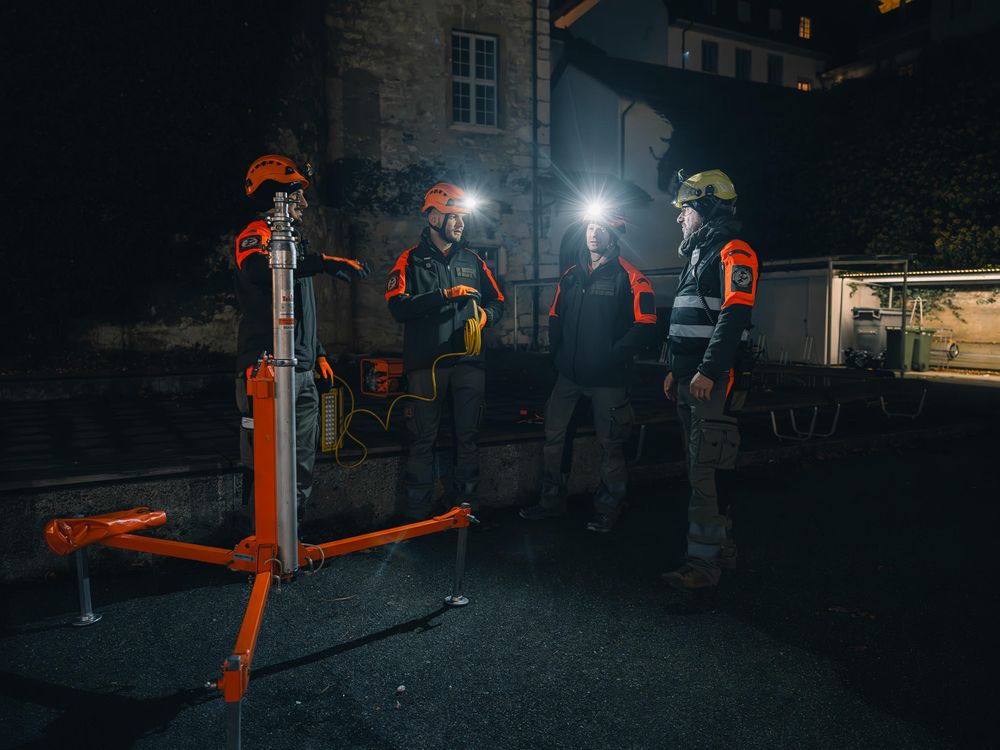Emergency workers in reflective gear gathered around portable lighting equipment at night.