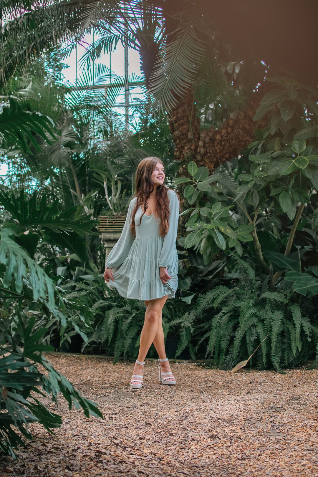 A fashion portrait in a lush greenhouse setting with tropical plants and soft lighting.