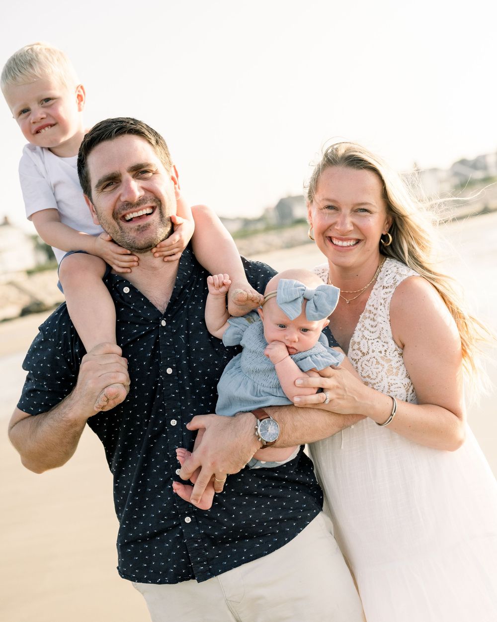 A joyful family shares candid moments together on a sunny beach, wearing coordinated navy polka dot and white outfits.