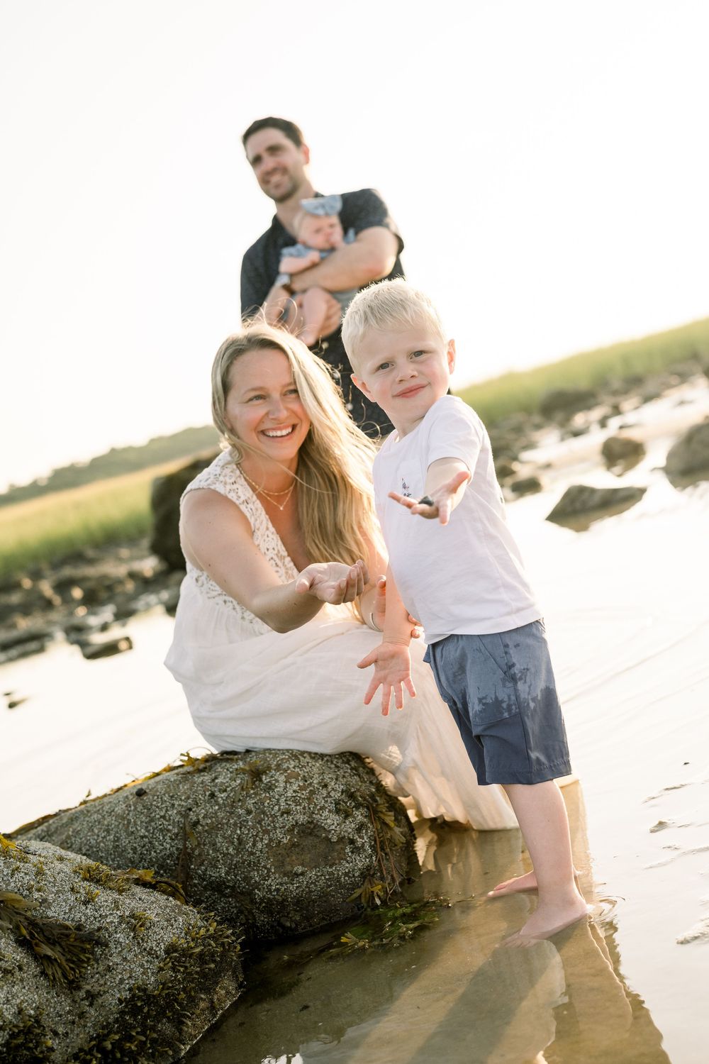 A family plays together on a sunny beach near large rocks at sunset.