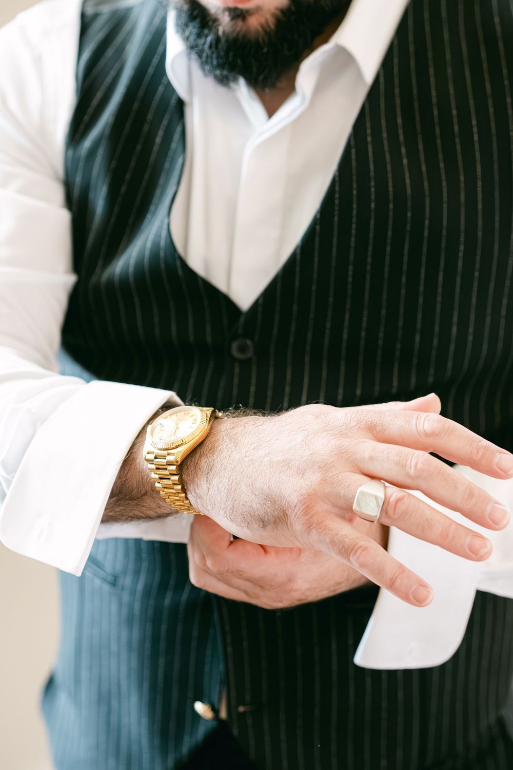 Close-up of hands wearing a pinstripe suit jacket and white dress shirt with gold watch detail.