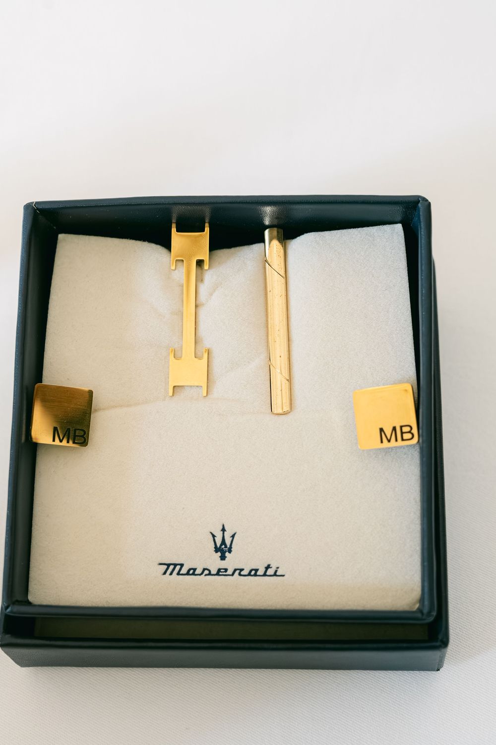 Gold-toned Maserati branded cufflinks displayed in a black presentation box with the iconic trident logo.
