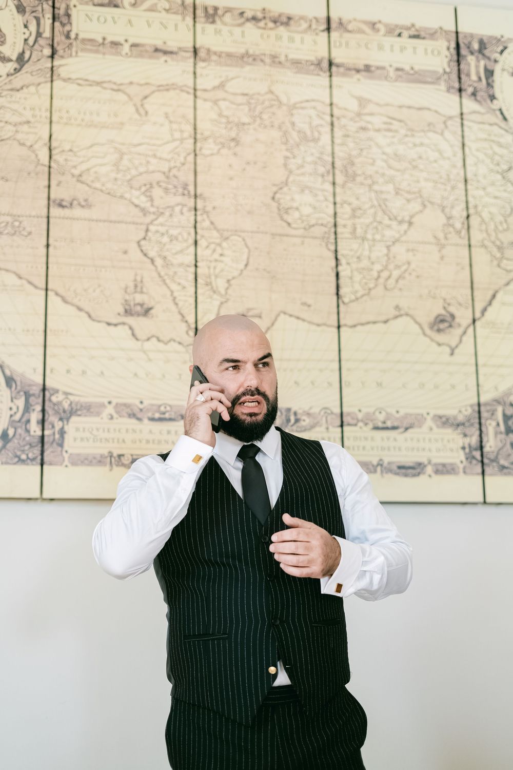 A series of photos showing someone in a pinstripe suit and white shirt posing against a wall with vintage maps.