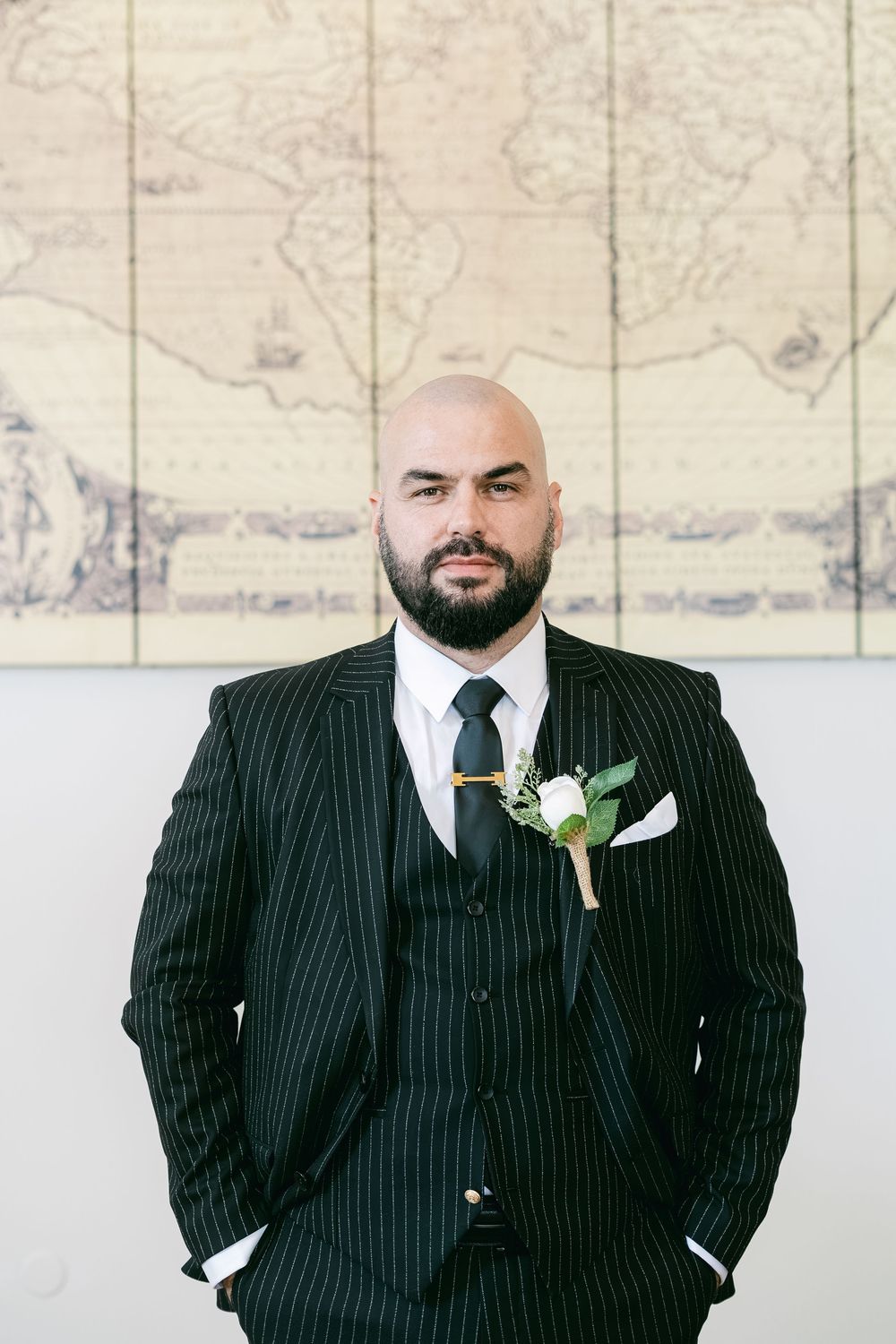 A person in a pinstripe suit with a white boutonniere poses in front of a light-colored wall.