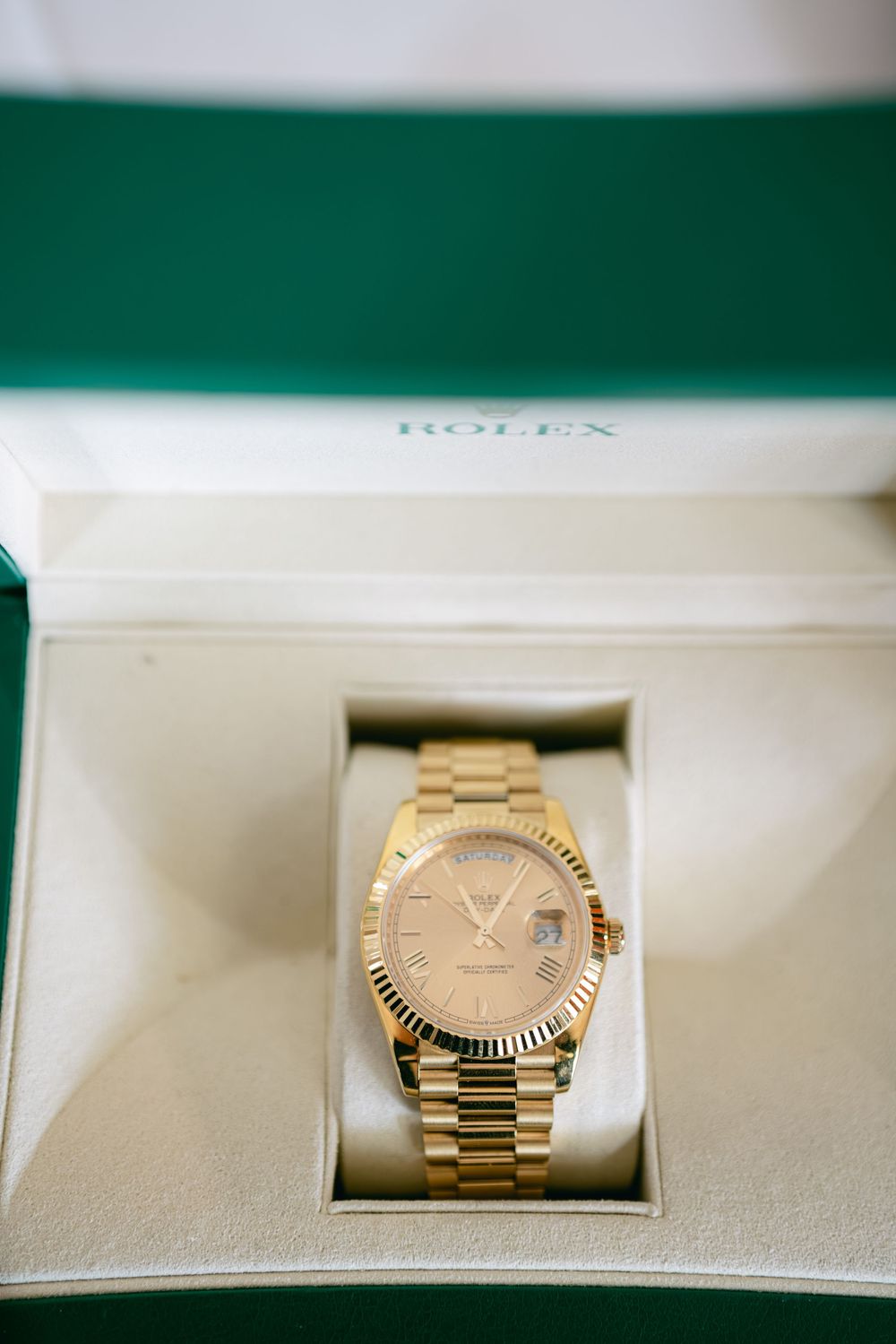 A gold Rolex Day-Date President watch with fluted bezel sits in a green leather presentation box.