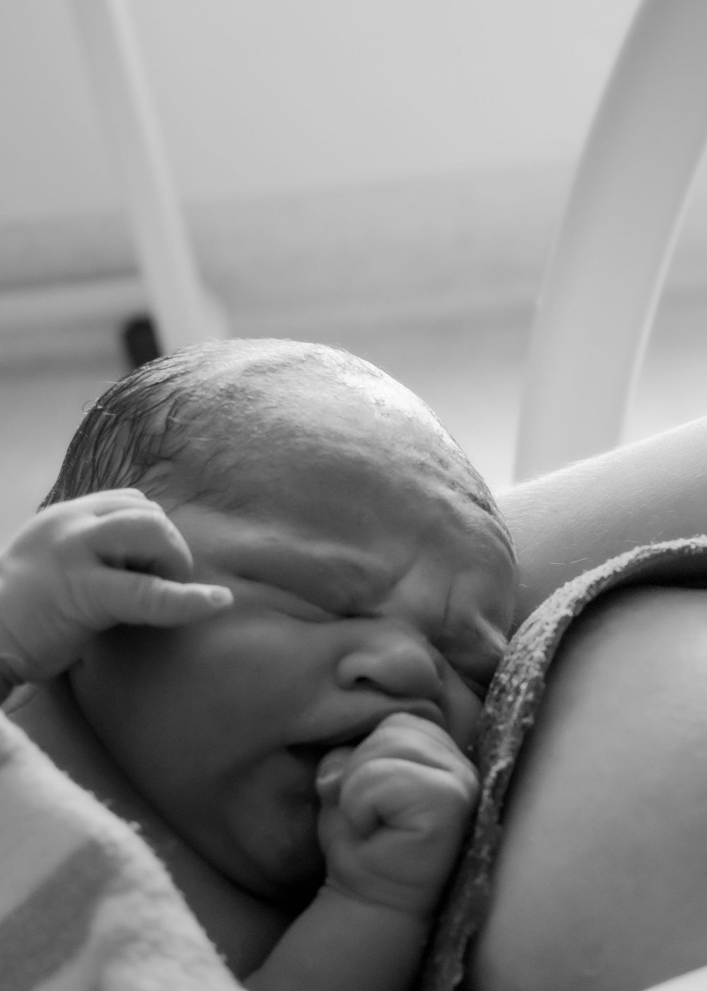 A newborn baby rests in black and white, sucking their thumb while being held against their mother during a central coast birth session.