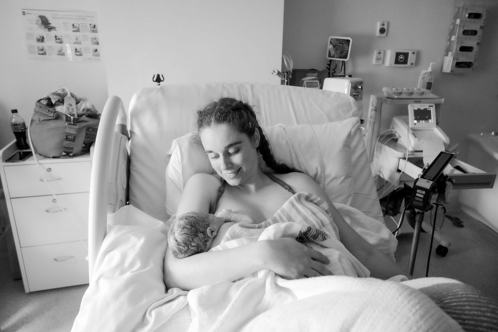 A tender moment in a hospital room as a parent holds their newborn baby in a black and white photograph during a central coast birth session