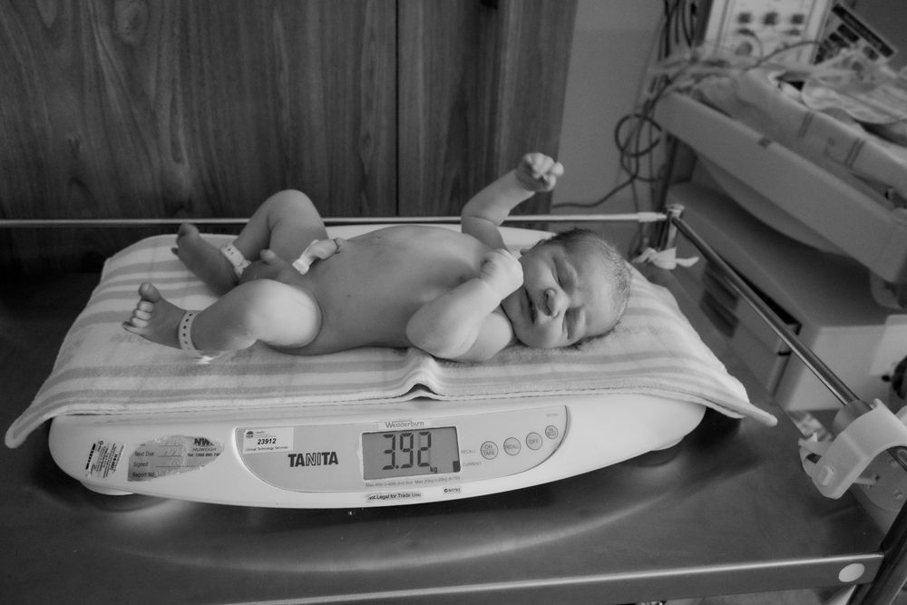 Newborn baby being weighed on a medical scale in black and white during a central coast birth session.