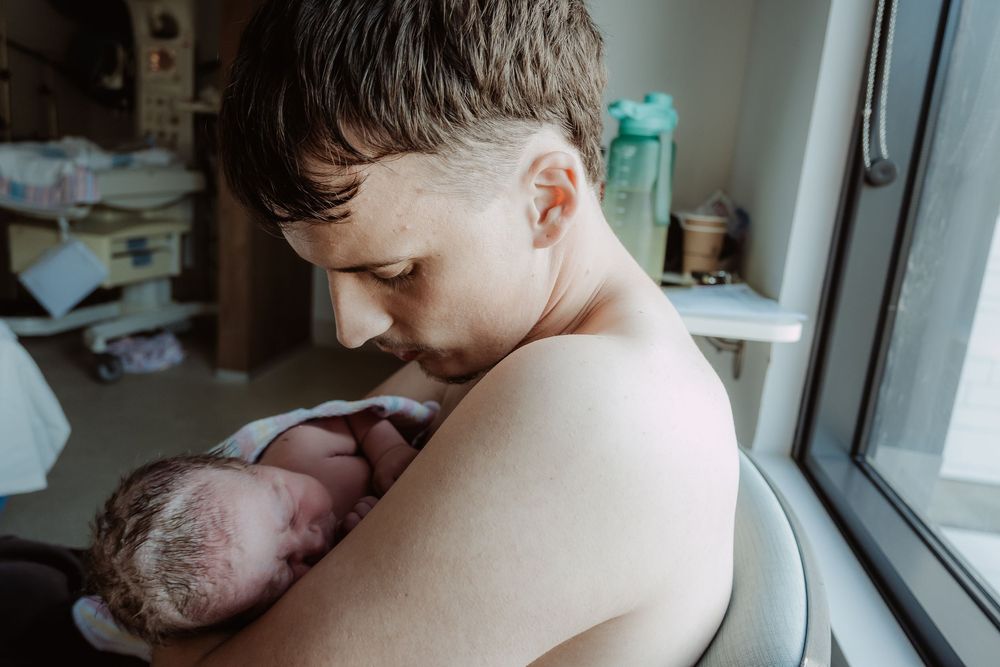 Tender moment of skin-to-skin contact between father and newborn during a central coast birth session.