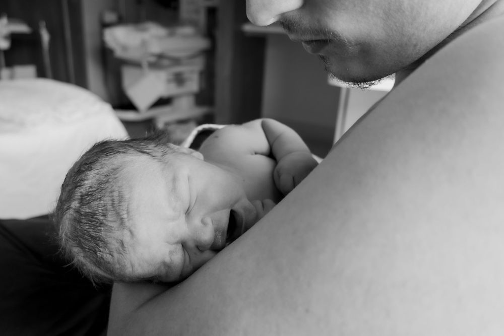 Close-up black and white moment of skin-to-skin contact between father and newborn during a central coast birth session.