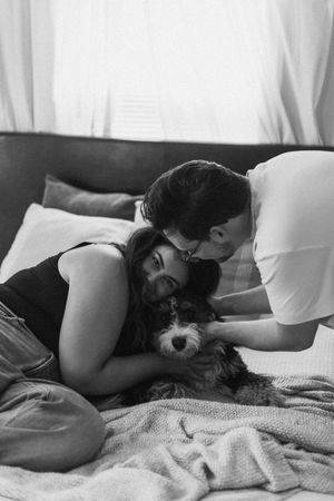 A couple shares tender moments together on a bed with white linens.