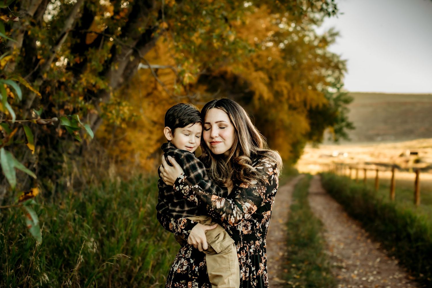 Couple embraces on a rustic dirt path surrounded by autumn trees during golden hour.
