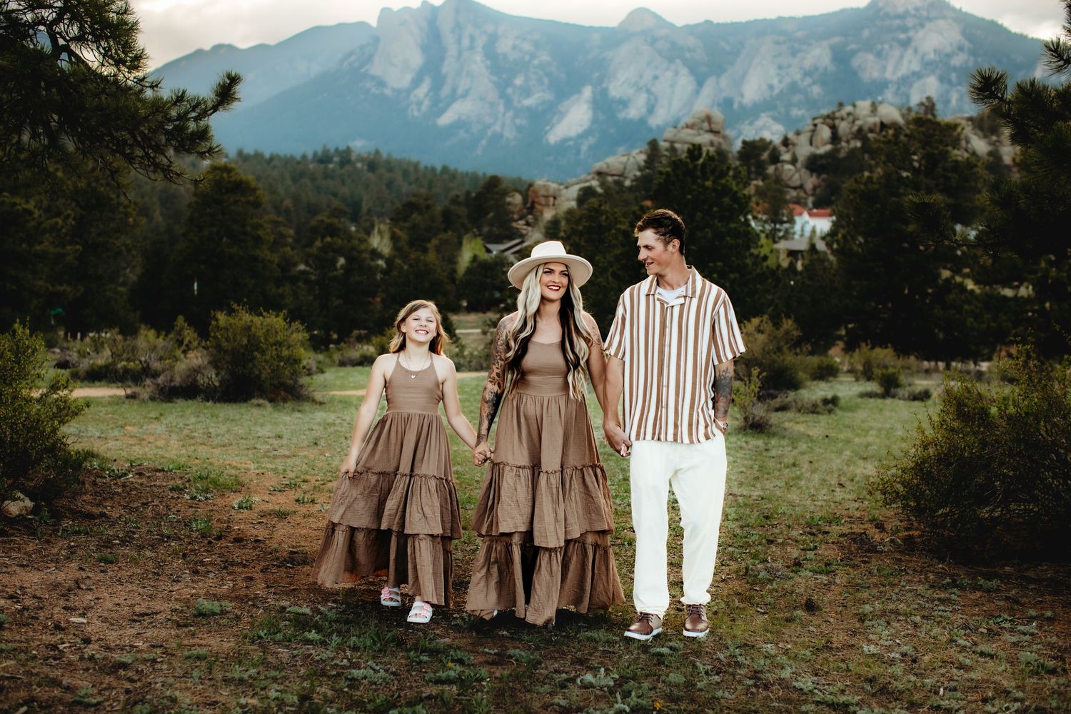 A group poses together on a grassy hillside with majestic mountain peaks rising in the background at sunset.