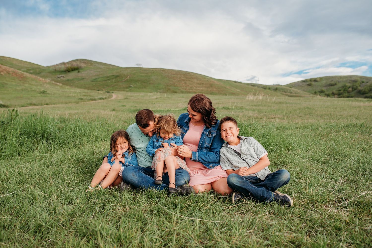 People lying together in a green rolling meadow under a cloudy sky on a summer day.