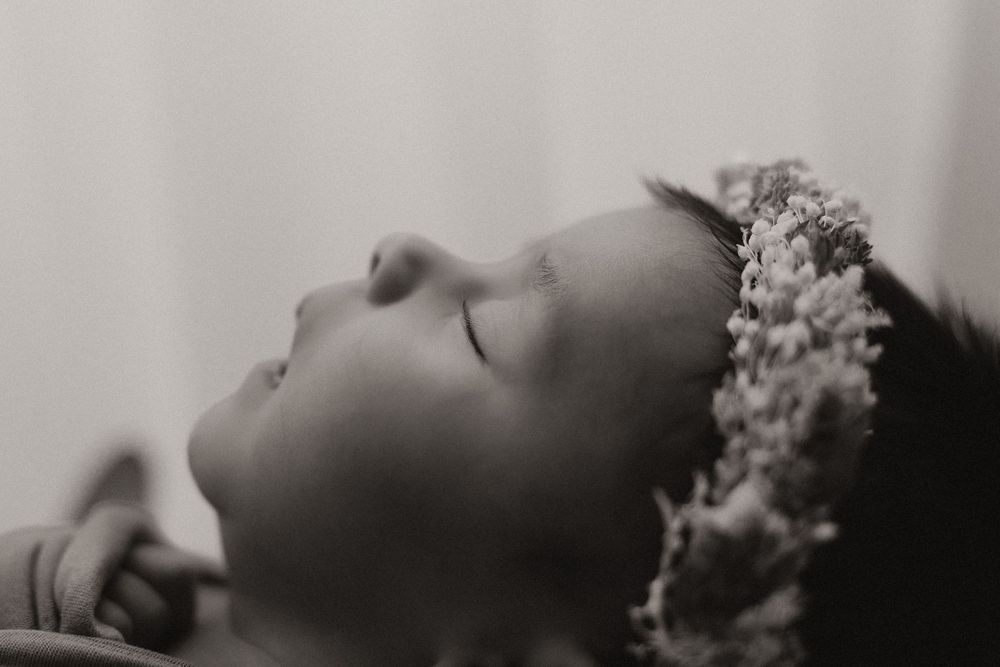 A black and white artistic profile portrait showing someone wearing a delicate floral headpiece while resting.