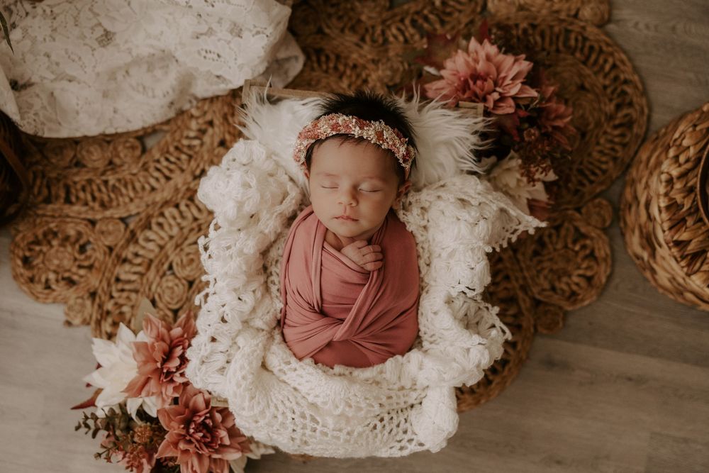 Newborn baby sleeping peacefully on white blanket with floral decorations in rustic setting.
