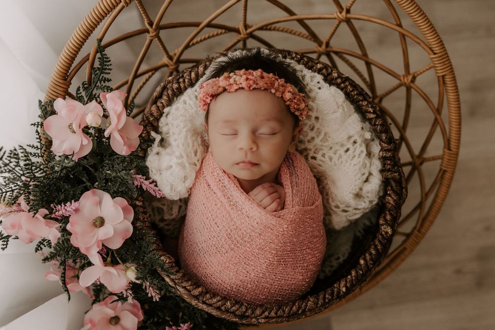 Collage of five newborn photography shots featuring a baby wrapped in pink swaddles with floral arrangements in woven baskets.