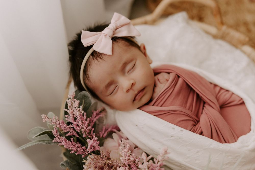 Newborn baby sleeping peacefully in pink swaddle with delicate cherry blossoms nearby.