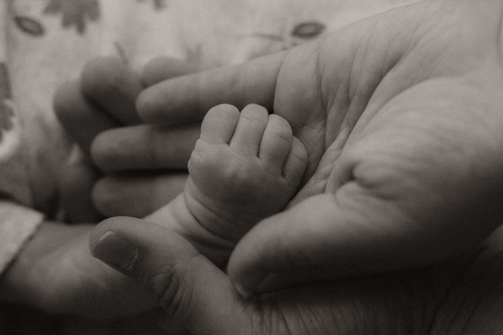 A sequence of black and white photographs showing hands gently holding and caressing a newborn baby's tiny feet.