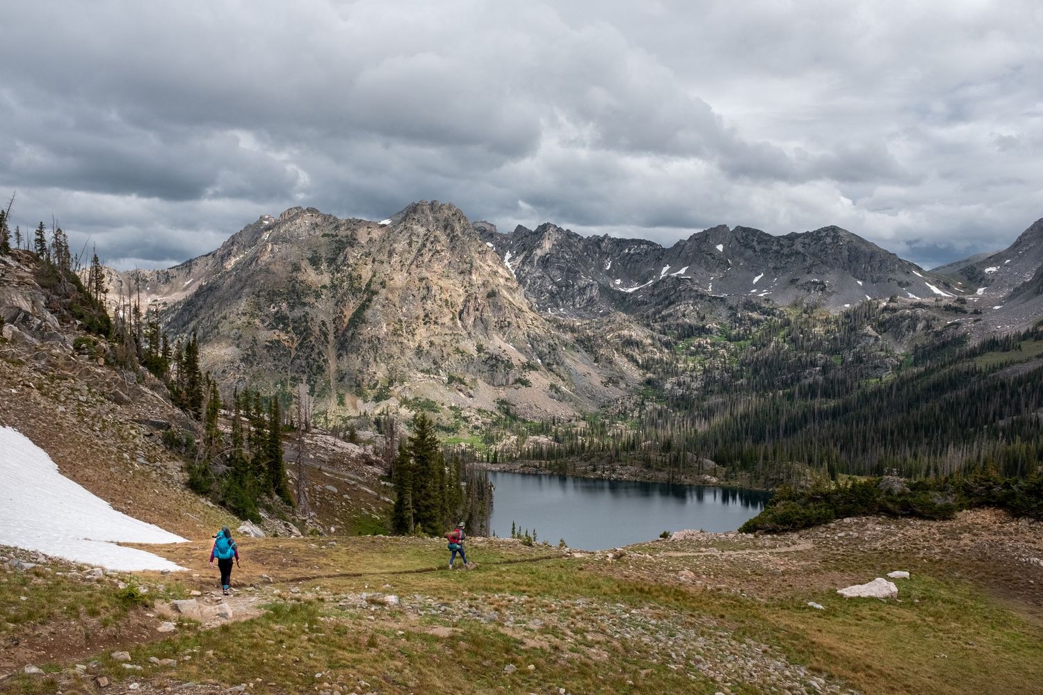 Panoramic mountain landscape with snow patches and a pristine alpine lake.