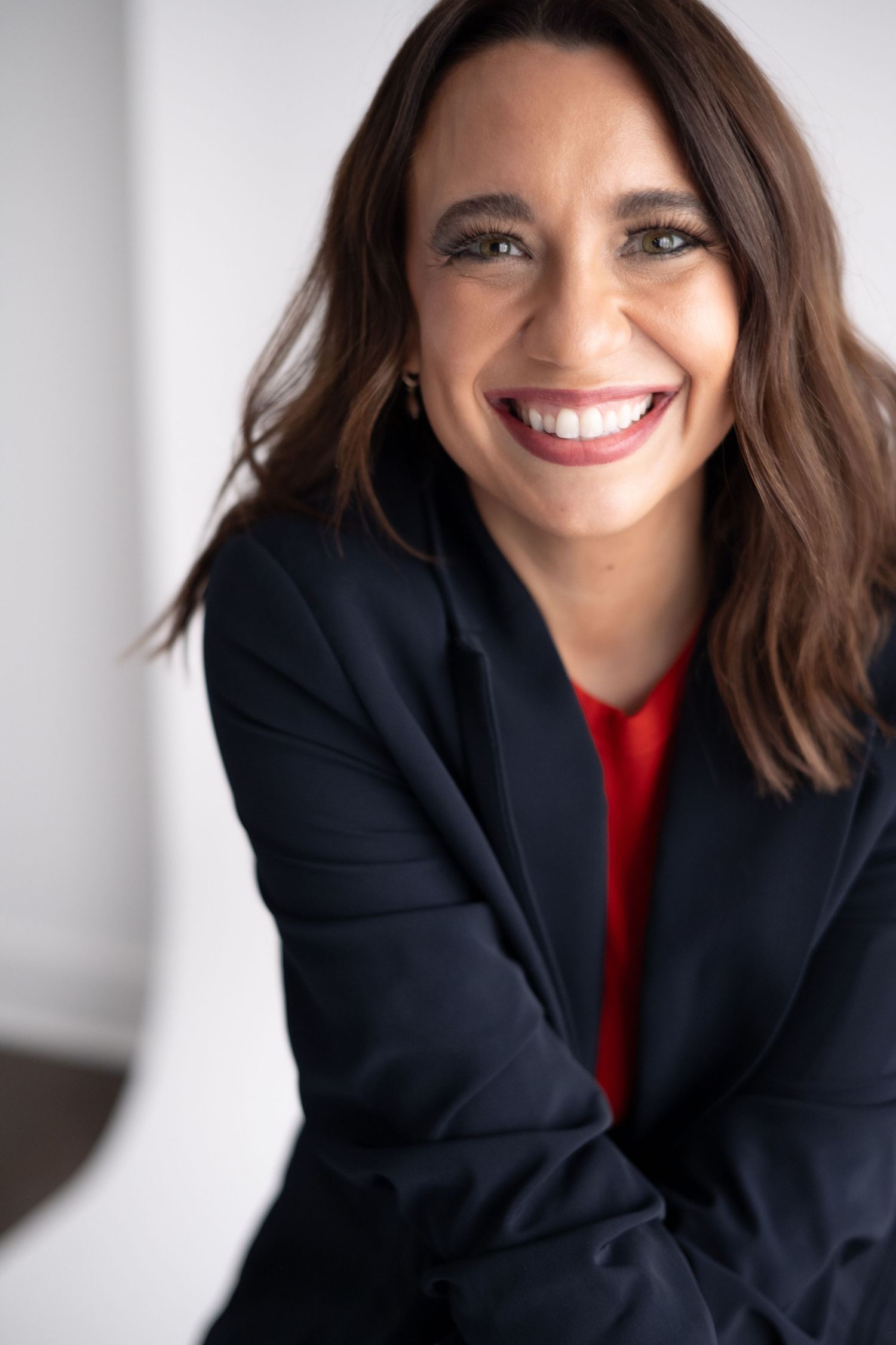 Professional headshot of someone in a navy blazer and red top smiling warmly against a light background.