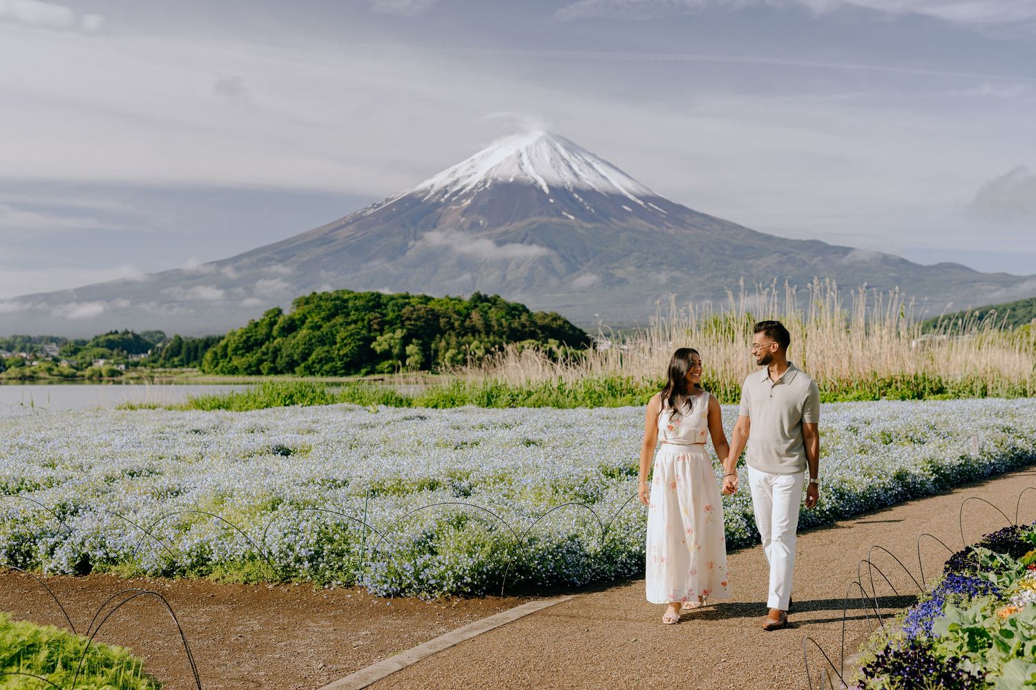 A couple walks on a path through blooming flowers with Mount Fuji rising majestically in the background.