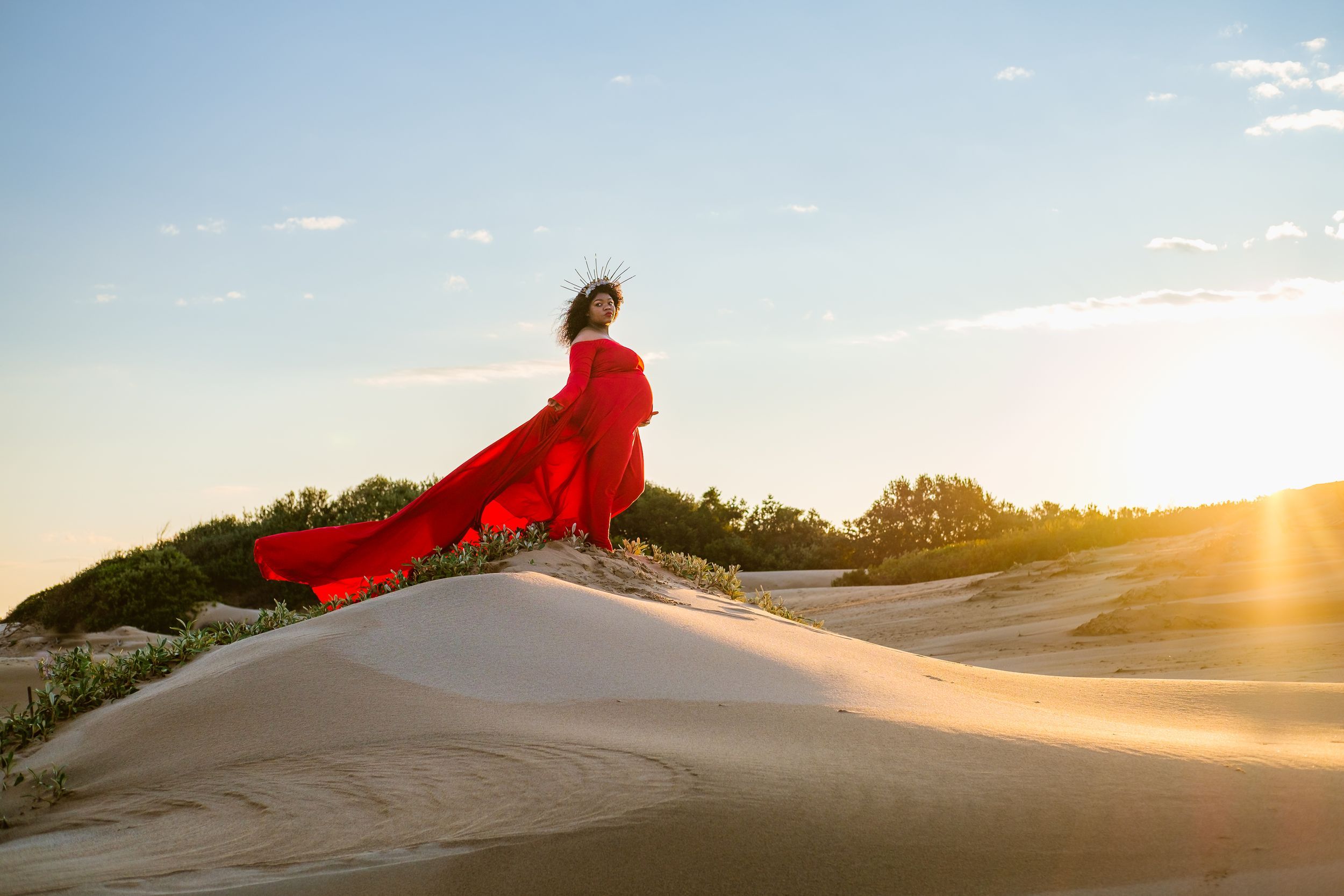 Maternity portrait in Mtunzini with a woman standing on a dune in a flowing red dress