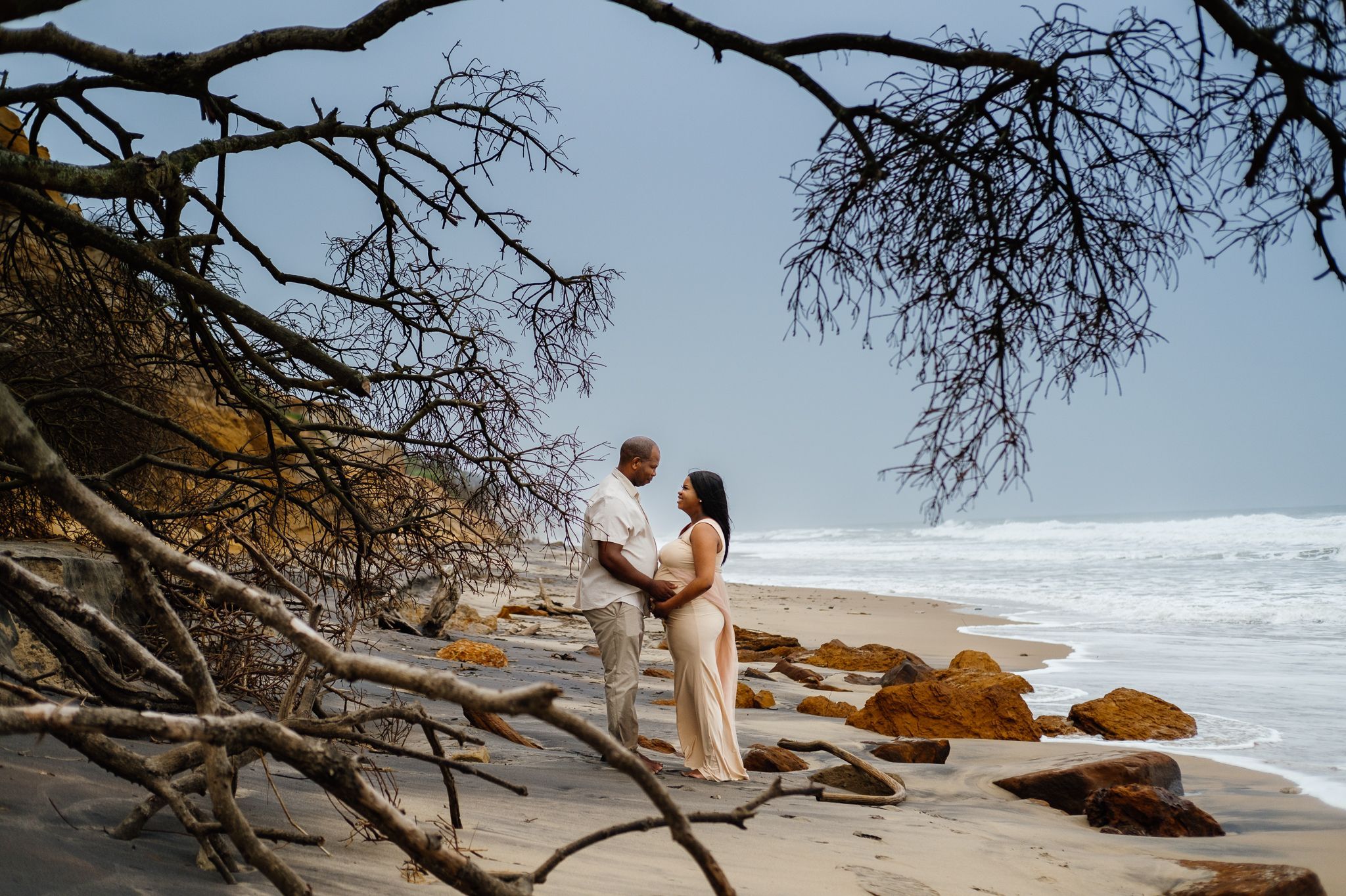Maternity couple framed by a fallen tree on Alkantstrand Beach